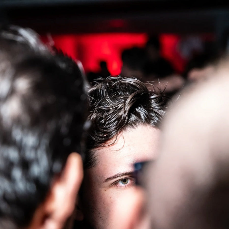 A crowd under red light, close on the back of one man's head.