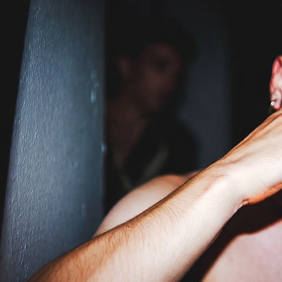 An arm braced against a blue-lit shower wall, a figure blurred behind.