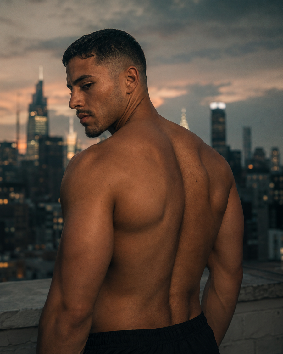 A man's bare back on a rooftop at dusk, city skyline behind.