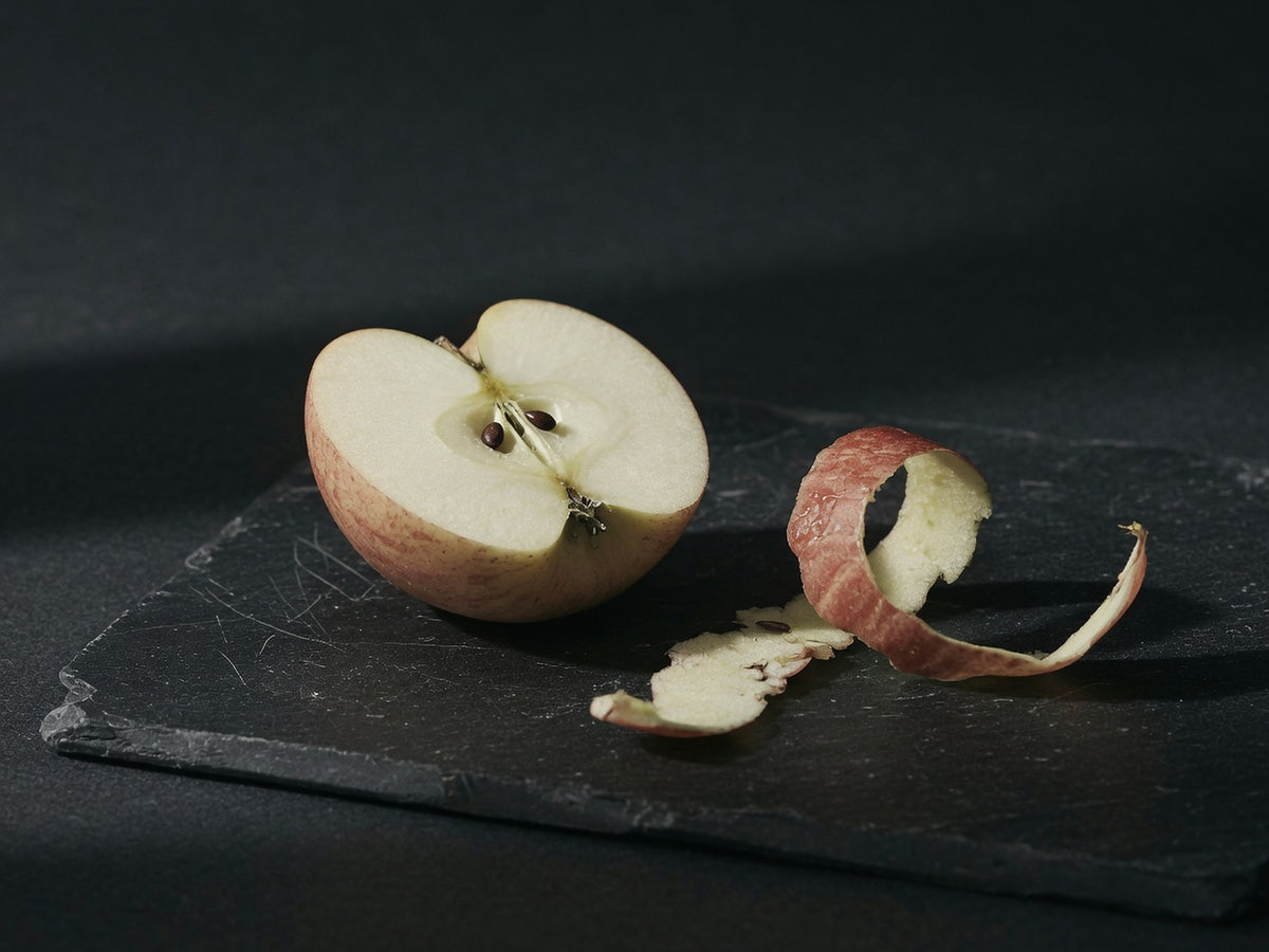 An apple halved to show pale flesh and pips, with a curl of peel beside it.