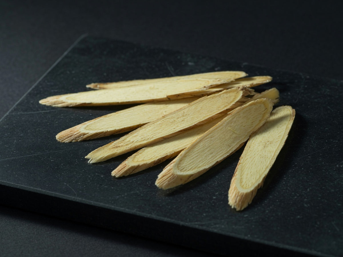 A fan of long flat pale yellow astragalus root slices with fine woody grain.