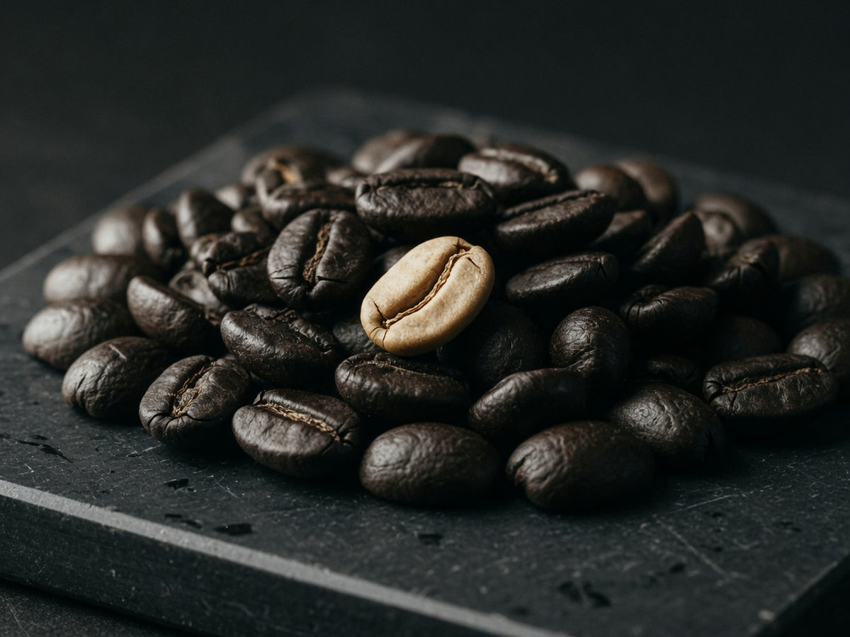 A tight cluster of dark oily roasted coffee beans, one split open.