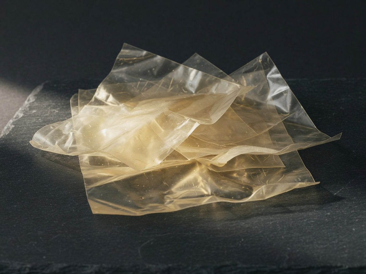 Translucent pale-gold leaf gelatin sheets, crumpled and overlapping.
