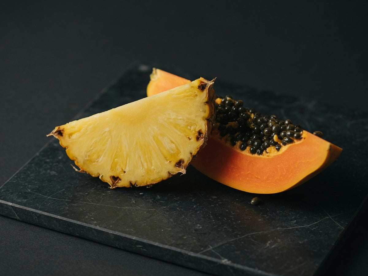A wedge of ripe pineapple beside a wedge of orange papaya with black seeds.