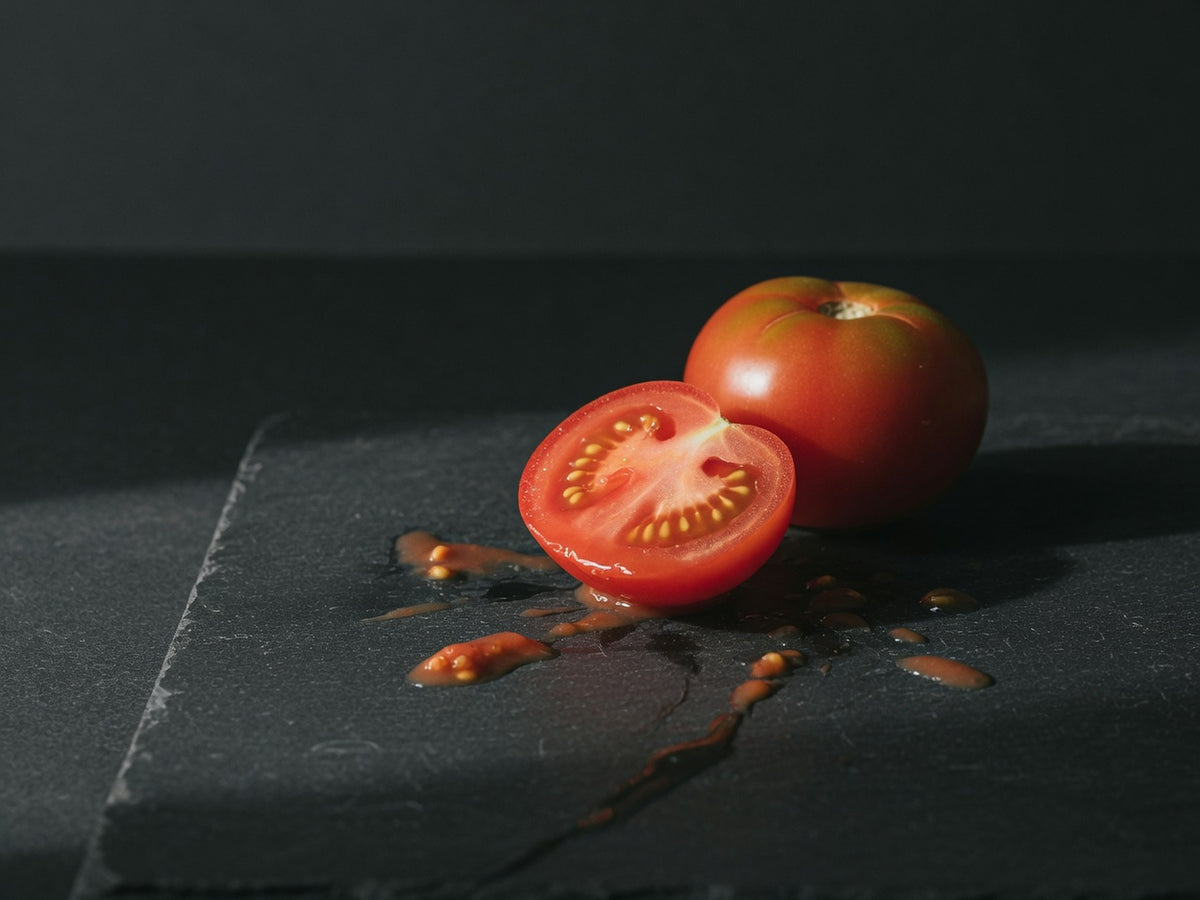 A ripe tomato cut in half, showing wet red flesh and seeds.