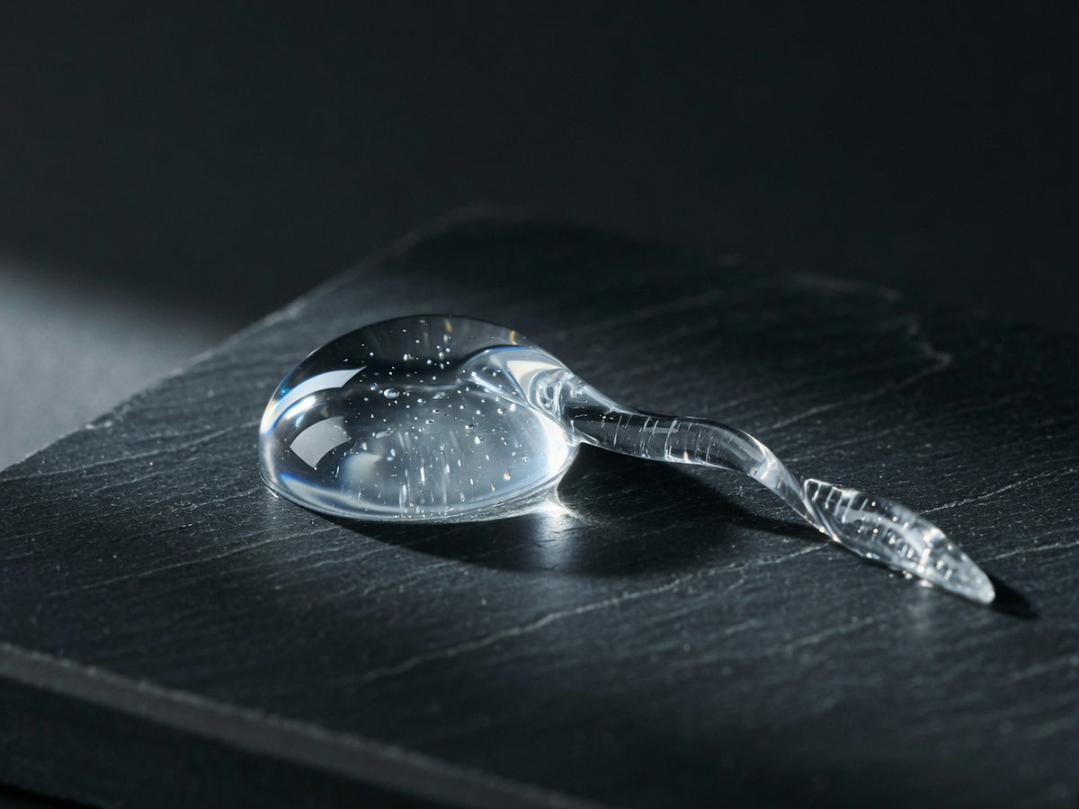 A glossy water-clear gel droplet and a short string of serum.
