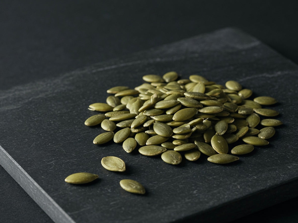 A loose heap of raw hulled pumpkin seeds, flat and green-olive.