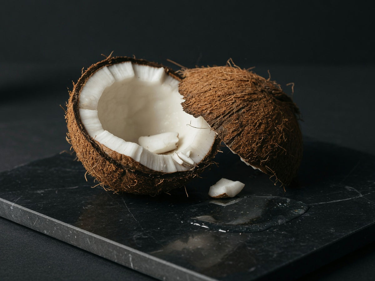 A cracked coconut: rough brown husk, white meat, and a small pool of clear oil.