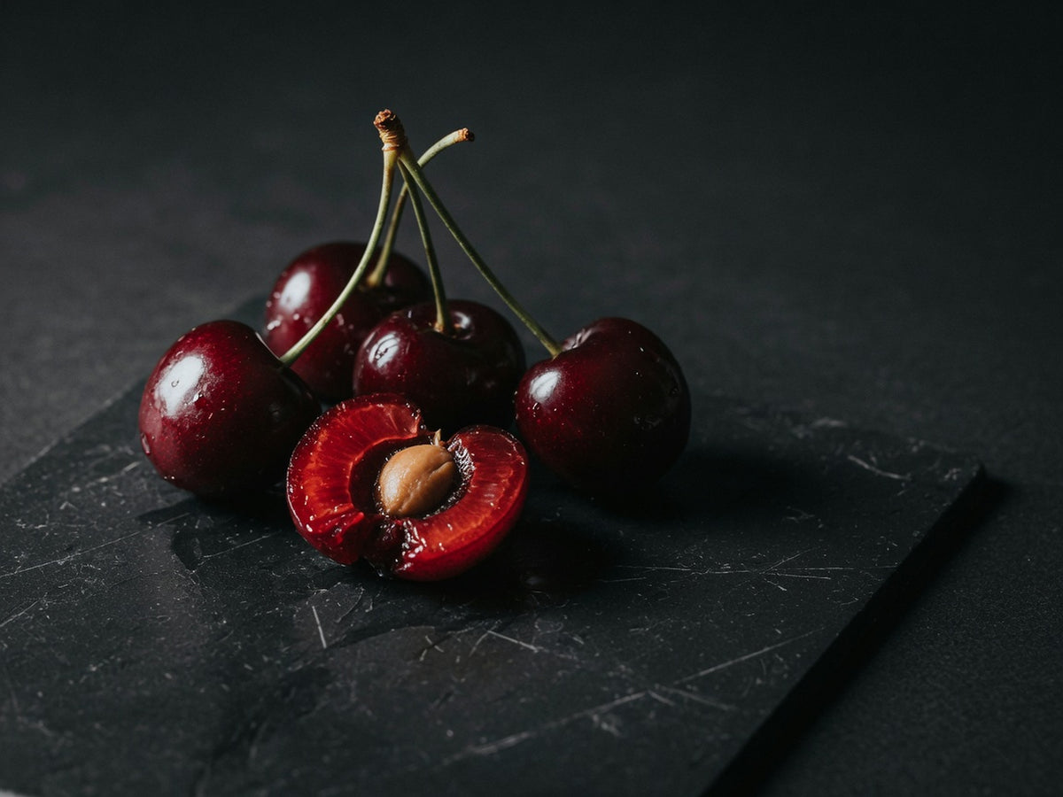 A cluster of glossy deep-red tart cherries with stems, one split to show the stone.