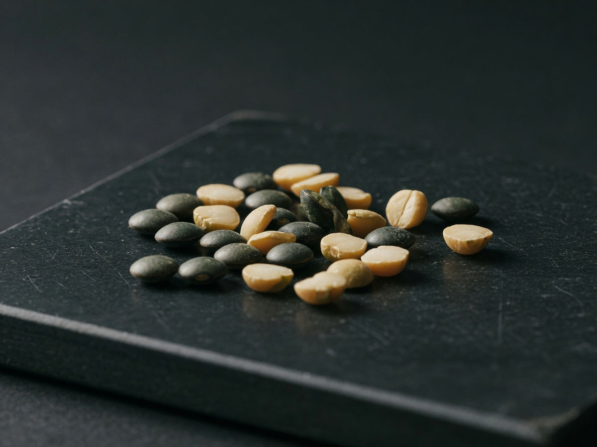 A small scatter of dark green lentils and pale split peas on black stone.