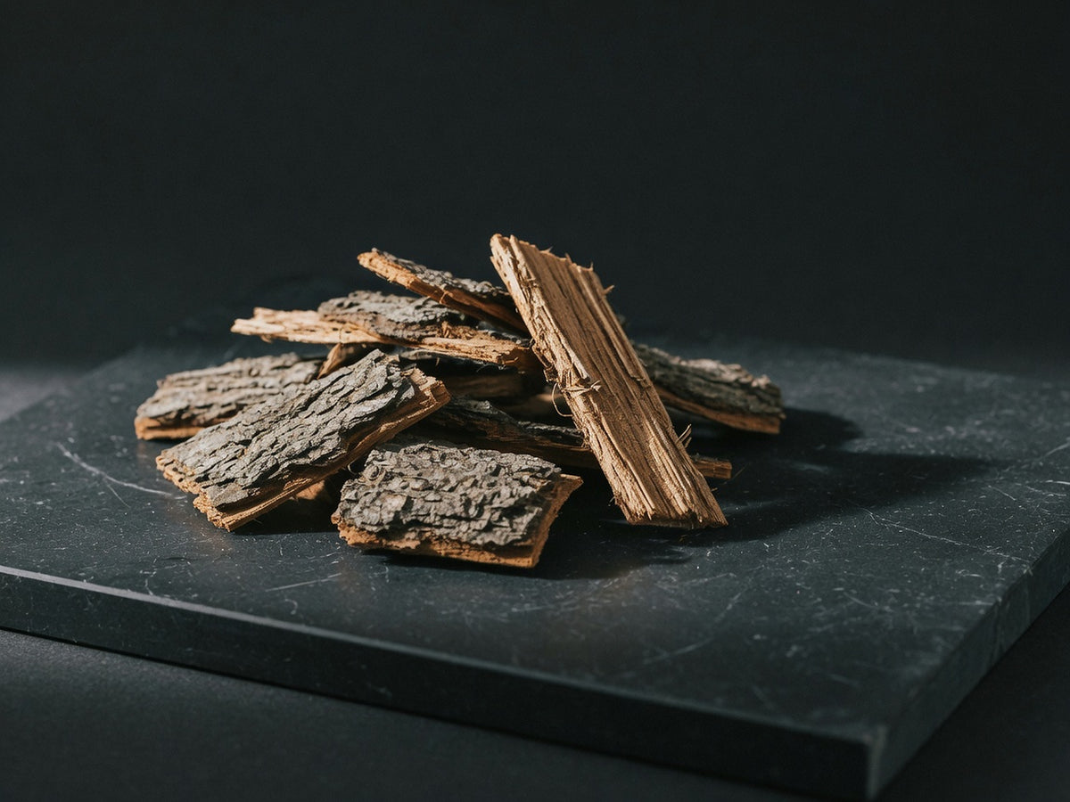 A small pile of coarse grey-brown muira puama bark chips with warm tan broken edges.