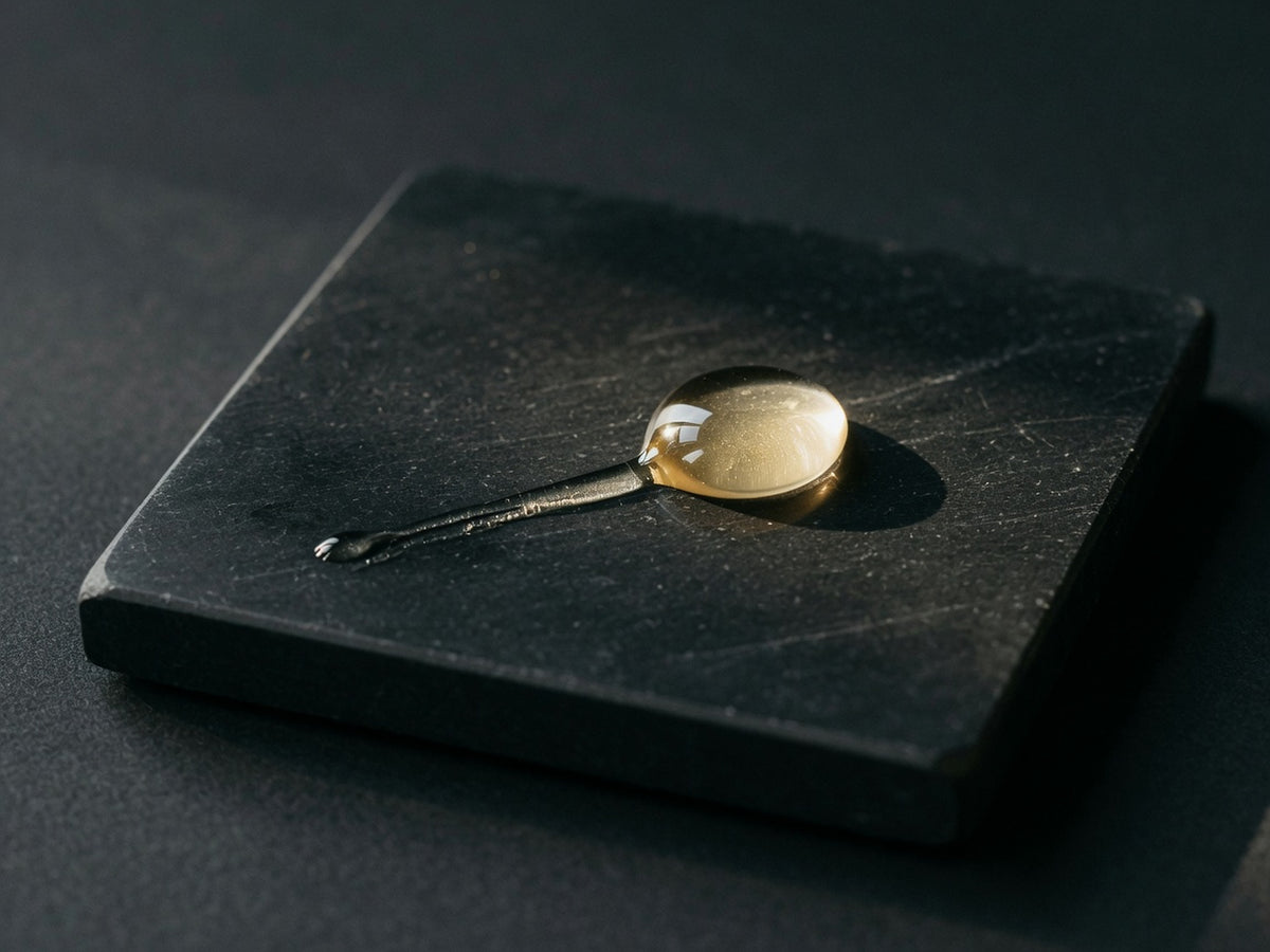 A glossy champagne-coloured droplet and trail of pale gold liquid.