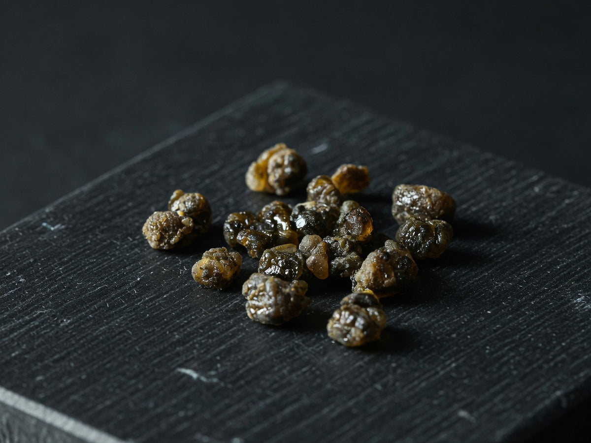 A cluster of dark olive-brown resinous granules, glossy and sticky.