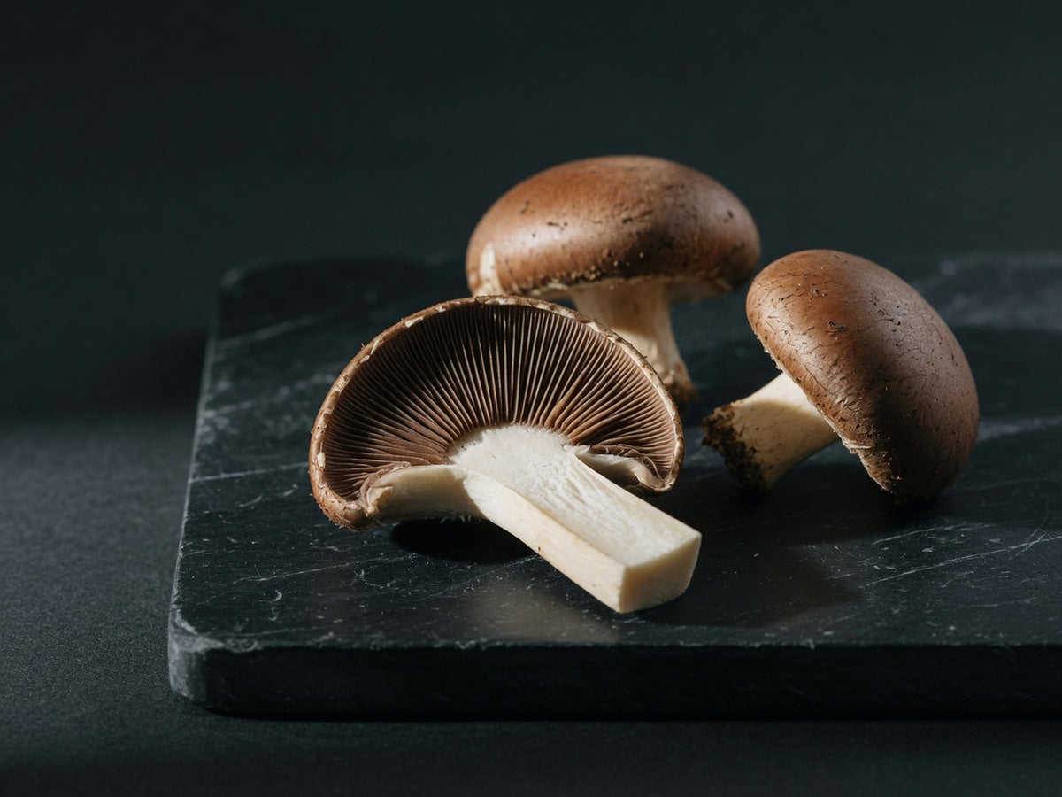 Chestnut mushrooms, one sliced lengthways to show its pale stem and dark radiating gills.