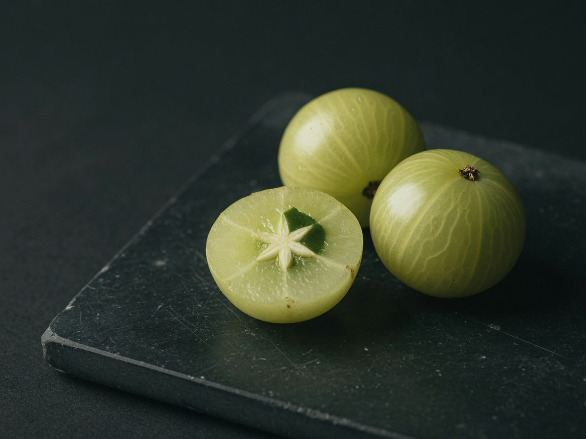 Three pale green amla fruits, one cut to show the star-shaped stone.