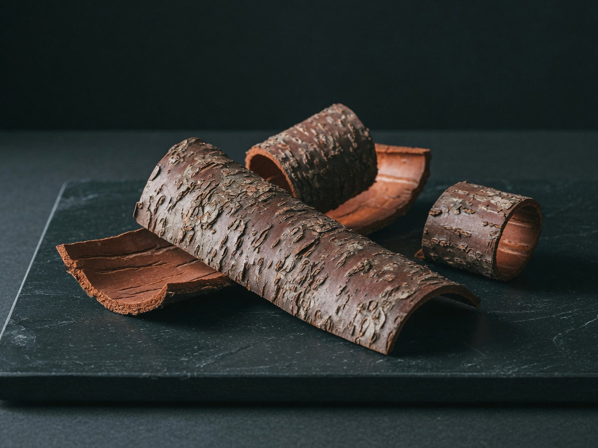 Three curled strips of reddish-brown African cherry bark on black stone.