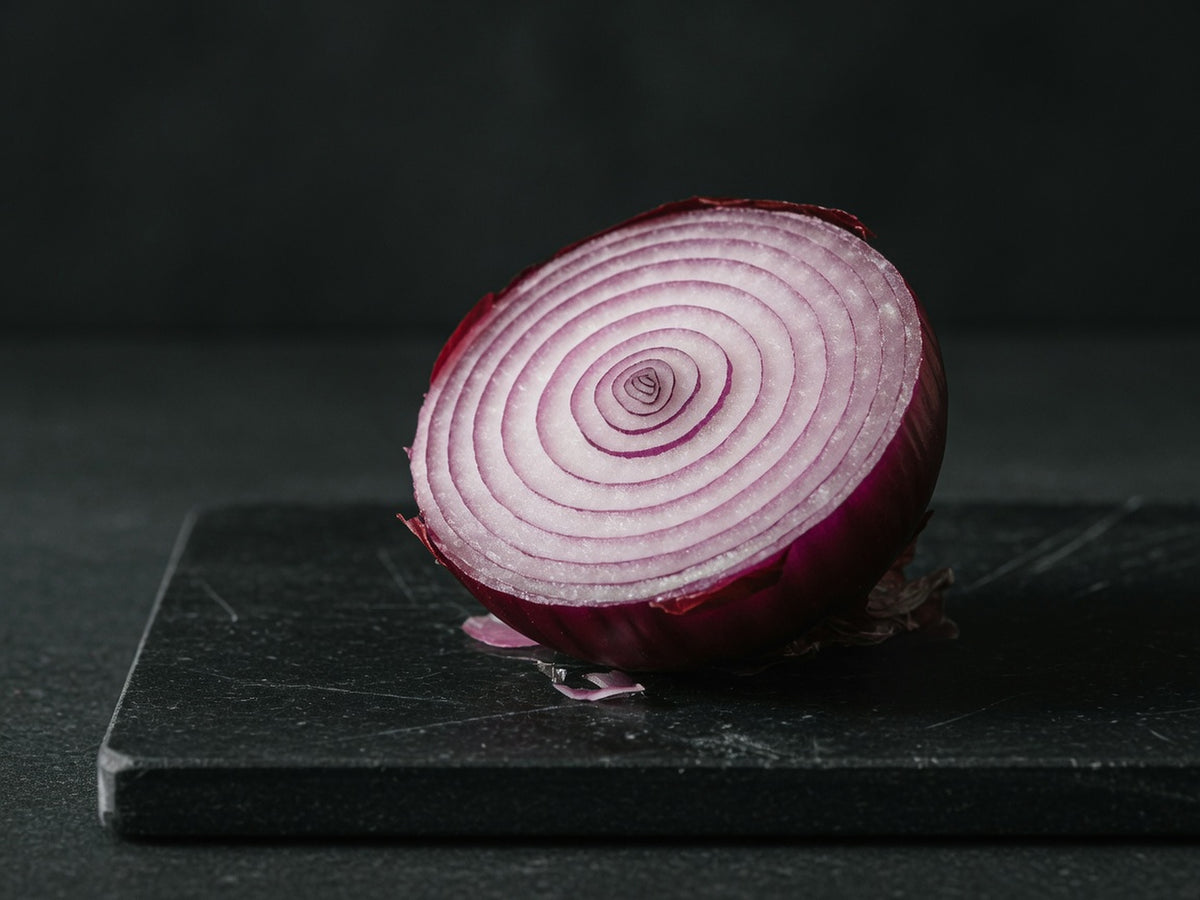 A red onion cut in half, showing tight purple concentric rings.