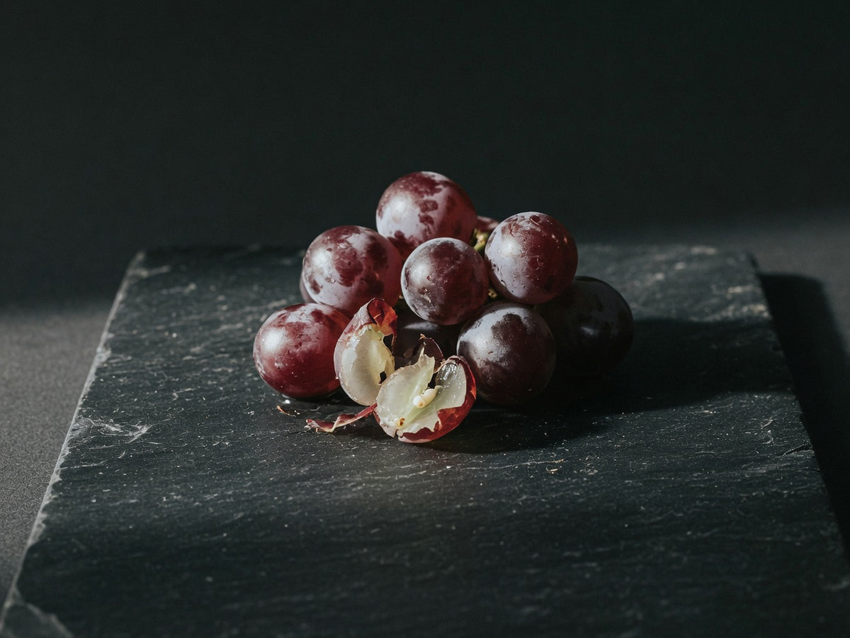 A cluster of dark red wine grapes with dusty bloom, one split open.