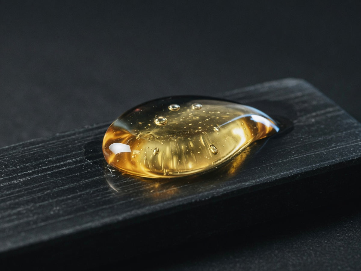 A glossy droplet of pale gold-amber oil serum.