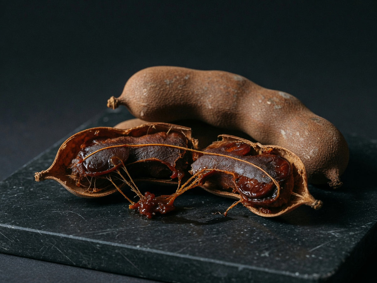 A tamarind pod split open to show sticky dark pulp and glossy seeds.