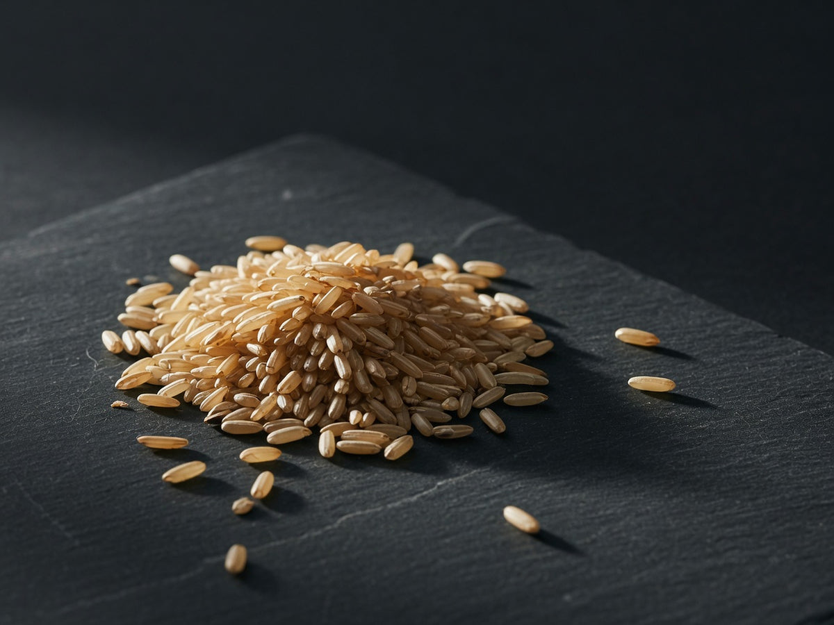 A small heap of whole brown rice grains with their husks on, warm tan and amber.