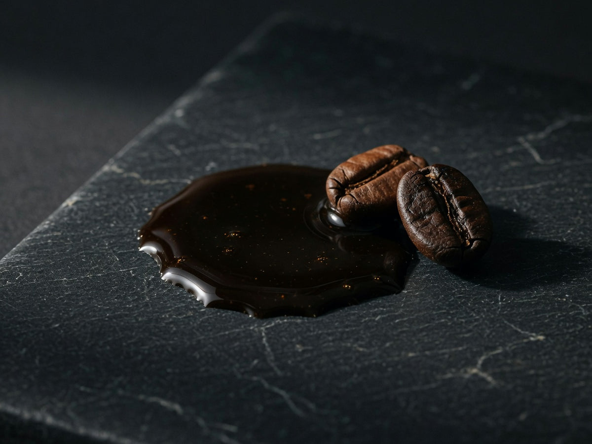 A viscous pool of black coffee extract beside two roasted beans.