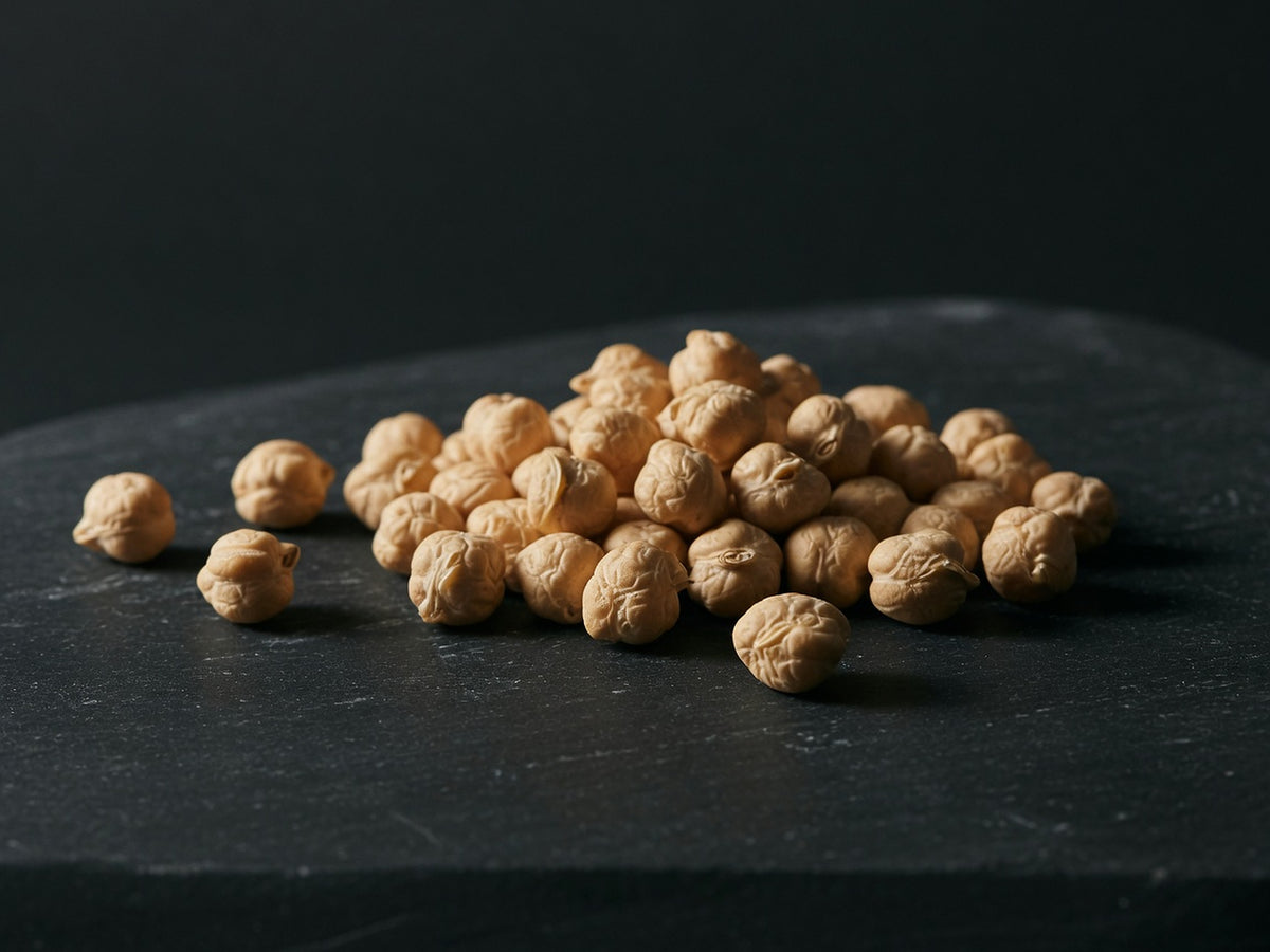 A loose heap of pale golden dried chickpeas on black stone.