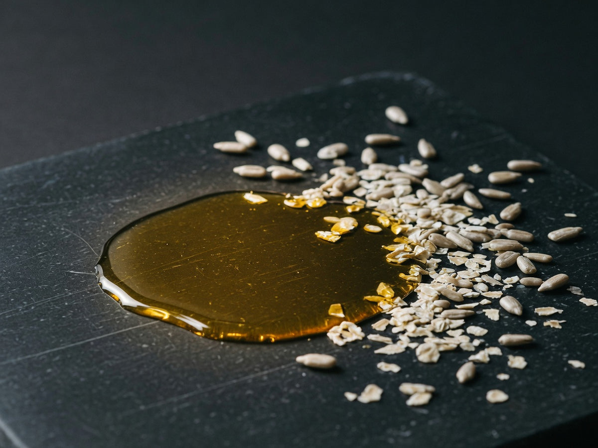 A pool of golden oil on black stone with wheat germ flakes and sunflower seeds at its edge.